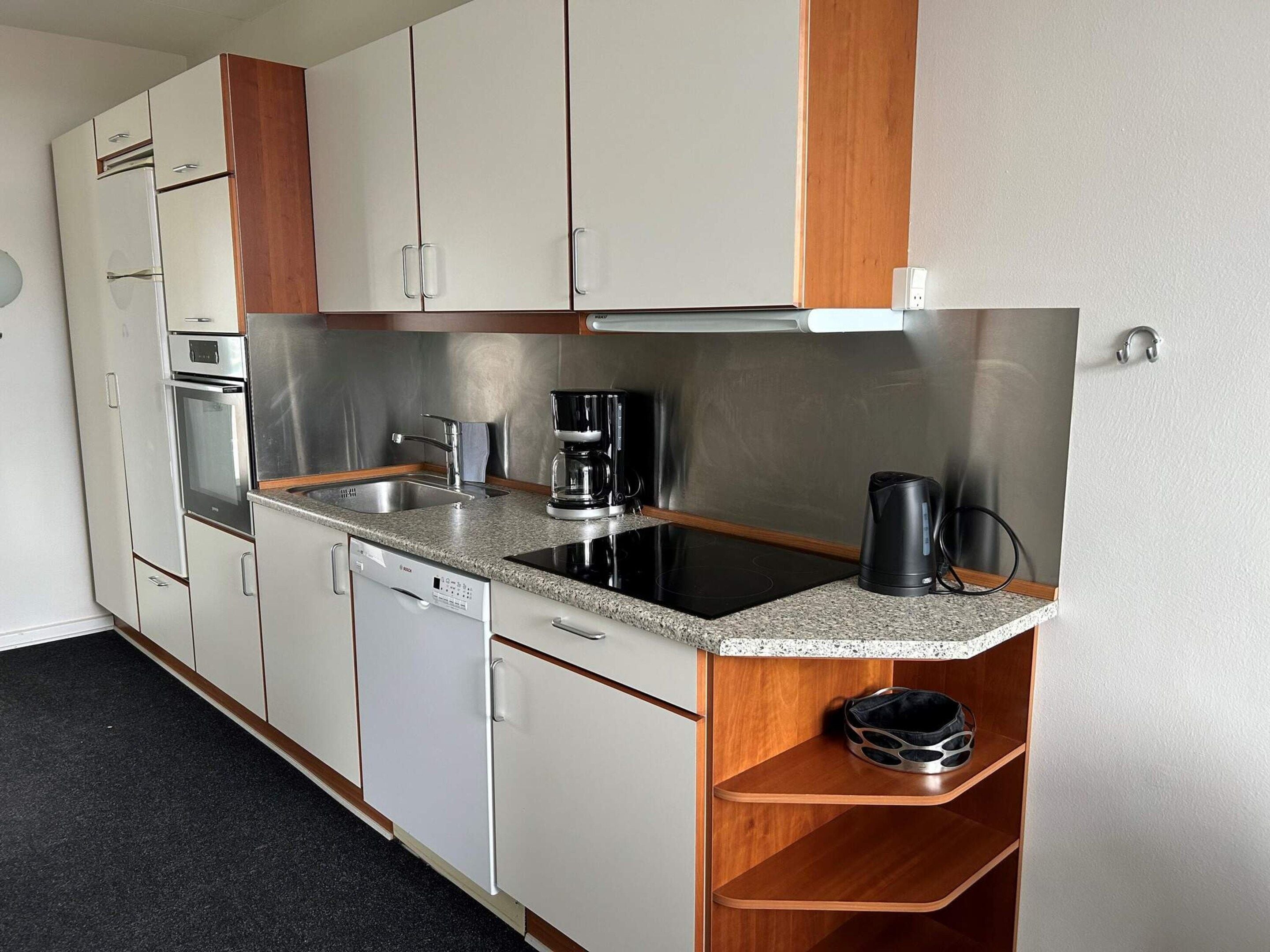 A compact kitchenette with a dishwasher, a coffee maker, and a kettle.