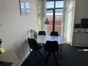 A room with a white table, four black chairs, a small white cabinet, a television, and a window with curtains.