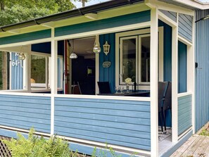 Ein blaues Haus mit Veranda, einem Esstisch, Stühlen und hängenden Leuchten.