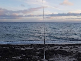 Una caña de pescar en una playa rocosa con el océano al fondo.