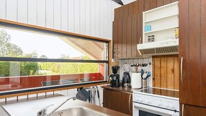 A modern kitchen with a stainless steel sink, wooden cabinets, a built-in oven, and a window overlooking a garden.