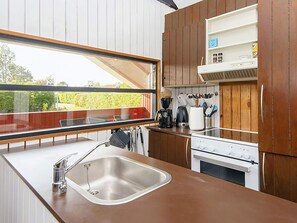 Une cuisine moderne dotée d’un évier en acier inoxydable, de meubles en bois, d’un four encastré et d’une fenêtre donnant sur un jardin.