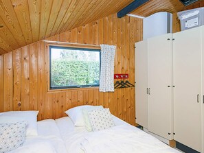 A bedroom with a wooden ceiling, a window with a view of greenery, a bed with patterned pillows, and a white wardrobe. - 6 Person Holiday Home in Sydals (Sydals)