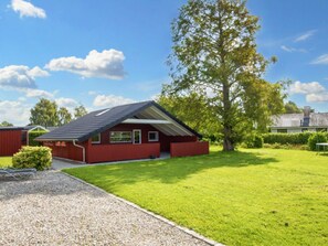 A red building with a sloped roof, surrounded by a well-maintained lawn and a large tree. - 6 Person Holiday Home in Sydals (Sydals)