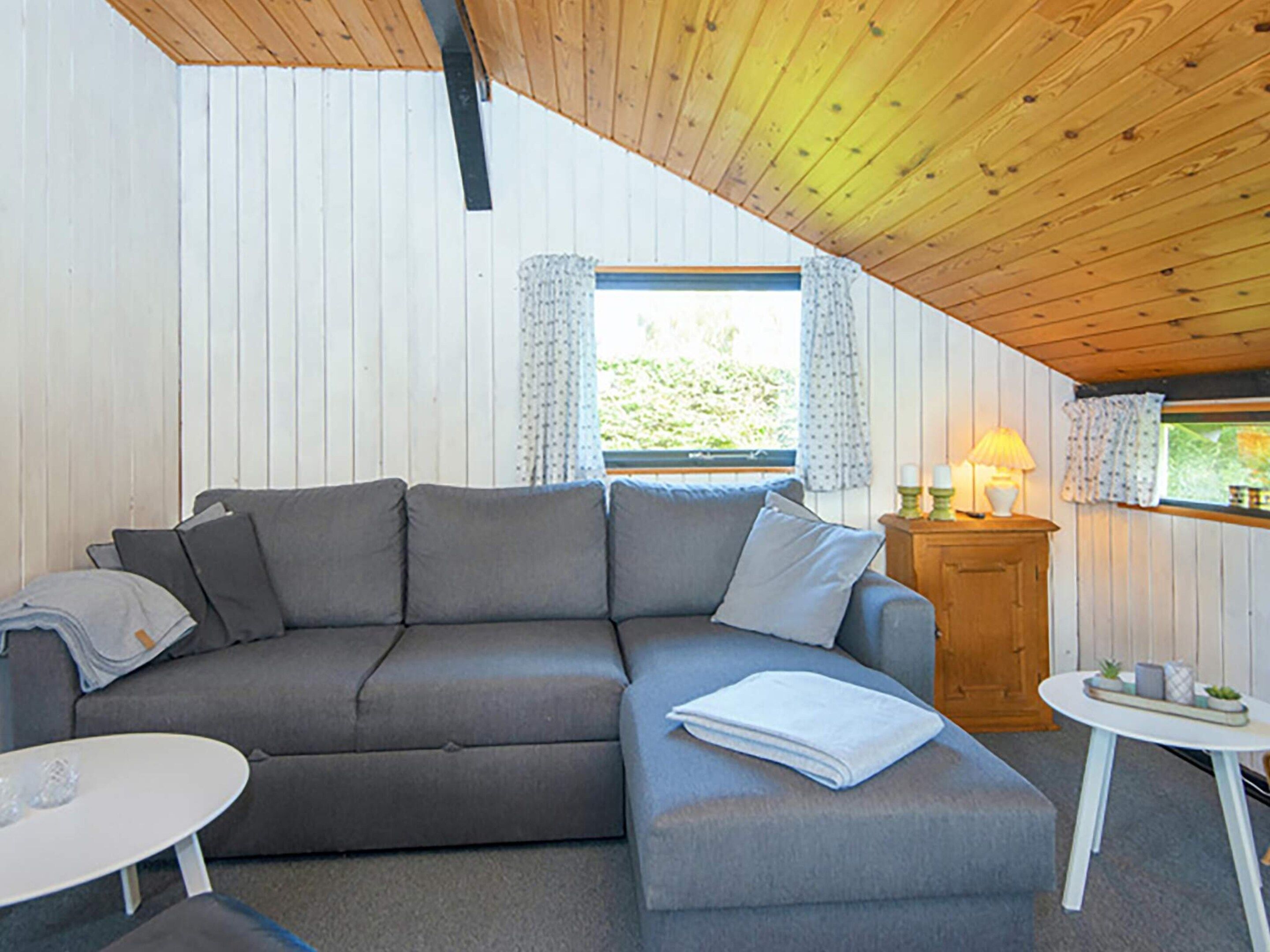 Ein gemütliches Zimmer mit einem grauen Ecksofa, einem kleinen weißen Tisch und einer Holzkabine mit einer Lampe.