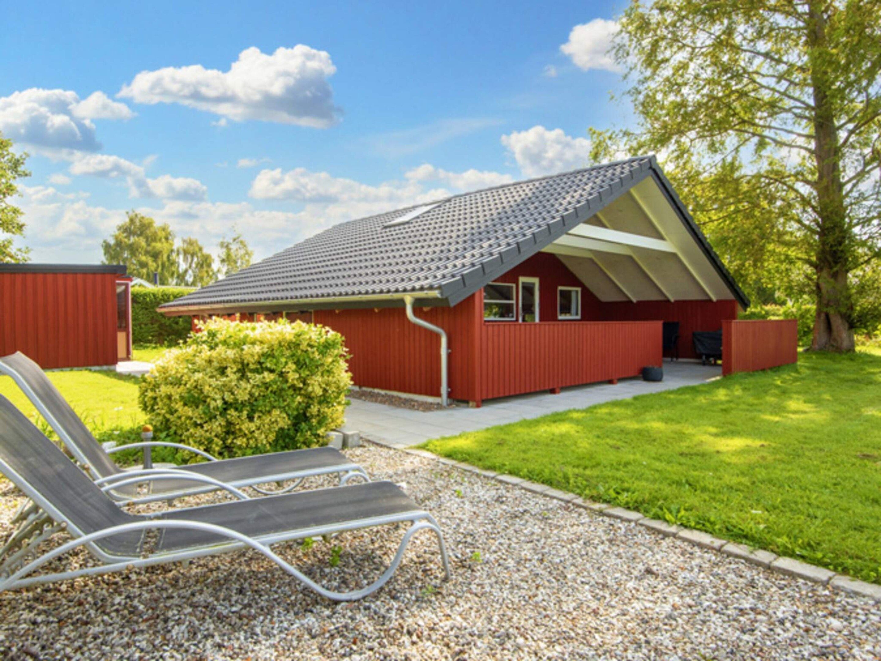 A red building with a sloped roof, a small porch, and a gravel path leading to a set of lounge chairs.