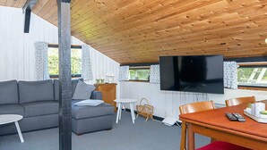 A cozy living room with a wooden ceiling, a grey sofa, a dining table with chairs, and a flat-screen TV mounted on the wall. - 6 Person Holiday Home in Sydals (Sydals)