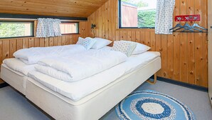 A wooden-paneled room with a large bed, two windows with curtains, and a blue and white patterned rug. - 6 Person Holiday Home in Sydals (Sydals)
