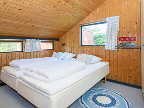 A wooden-paneled room with a large bed, two windows with curtains, and a blue and white patterned rug. - 6 Person Holiday Home in Sydals (Sydals)