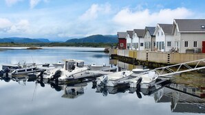 A marina with several boats docked, a wooden pier, and a row of houses with a mountain backdrop. - 6 Person Holiday Home in Bud (Averoy)