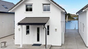 A white two-story house with a covered porch and a dock extending into a body of water. - 6 Person Holiday Home in Bud (Averoy)