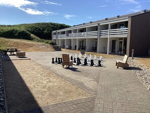 Un juego de ajedrez al aire libre sobre una superficie pavimentada, con bancos y un edificio al fondo.