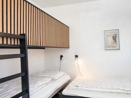 Un letto a castello con testiera a listelli, un comodino con una lampada e un quadro astratto incorniciato appeso al muro.