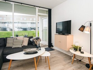 A modern living room with a large window, a black sofa, a white coffee table, a television, and a small side table with a lamp and decorative items.