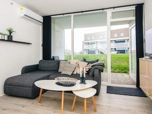 A modern living room with a grey sofa, a white table with a decorative bowl, and a view of a building through a glass door.