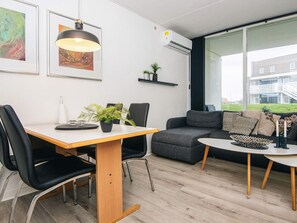 A modern living room with a dining table, chairs, a sofa, and a large window offering a view of buildings outside.