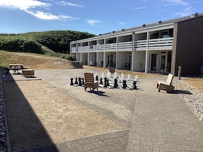 A chessboard set up on a paved area with benches and a building in the background.