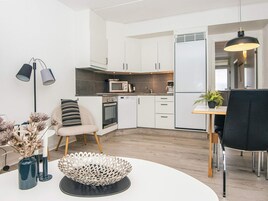 Uma cozinha moderna com armários brancos, micro-ondas, forno e frigorífico. Há uma área de jantar com uma mesa, cadeiras e um vaso de planta.