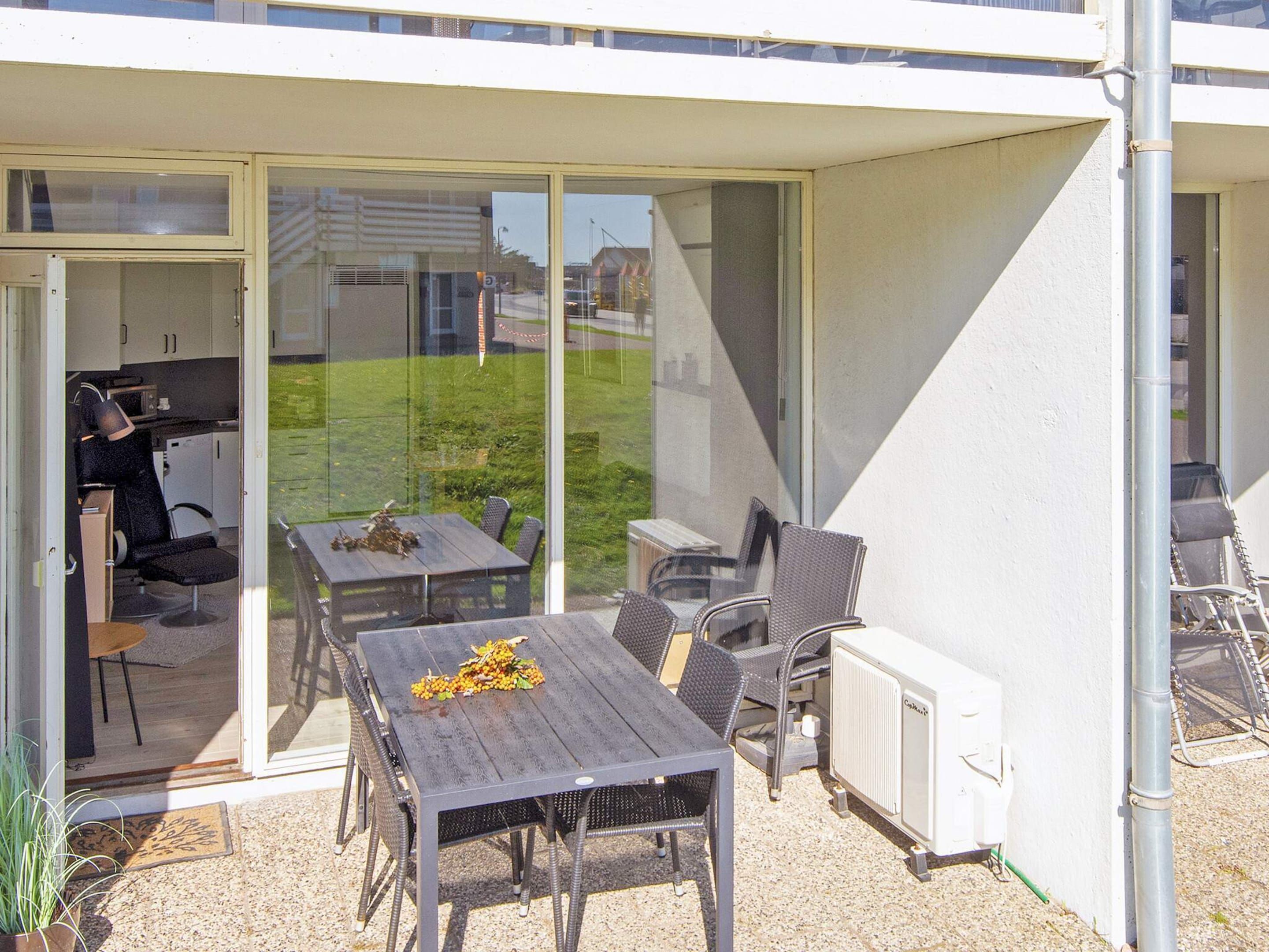 Une terrasse extérieure avec une table et des chaises, un radiateur et une porte vitrée donnant sur une cuisine.