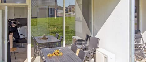 An outdoor patio with a table and chairs, a radiator, and a glass door leading to a kitchen.
