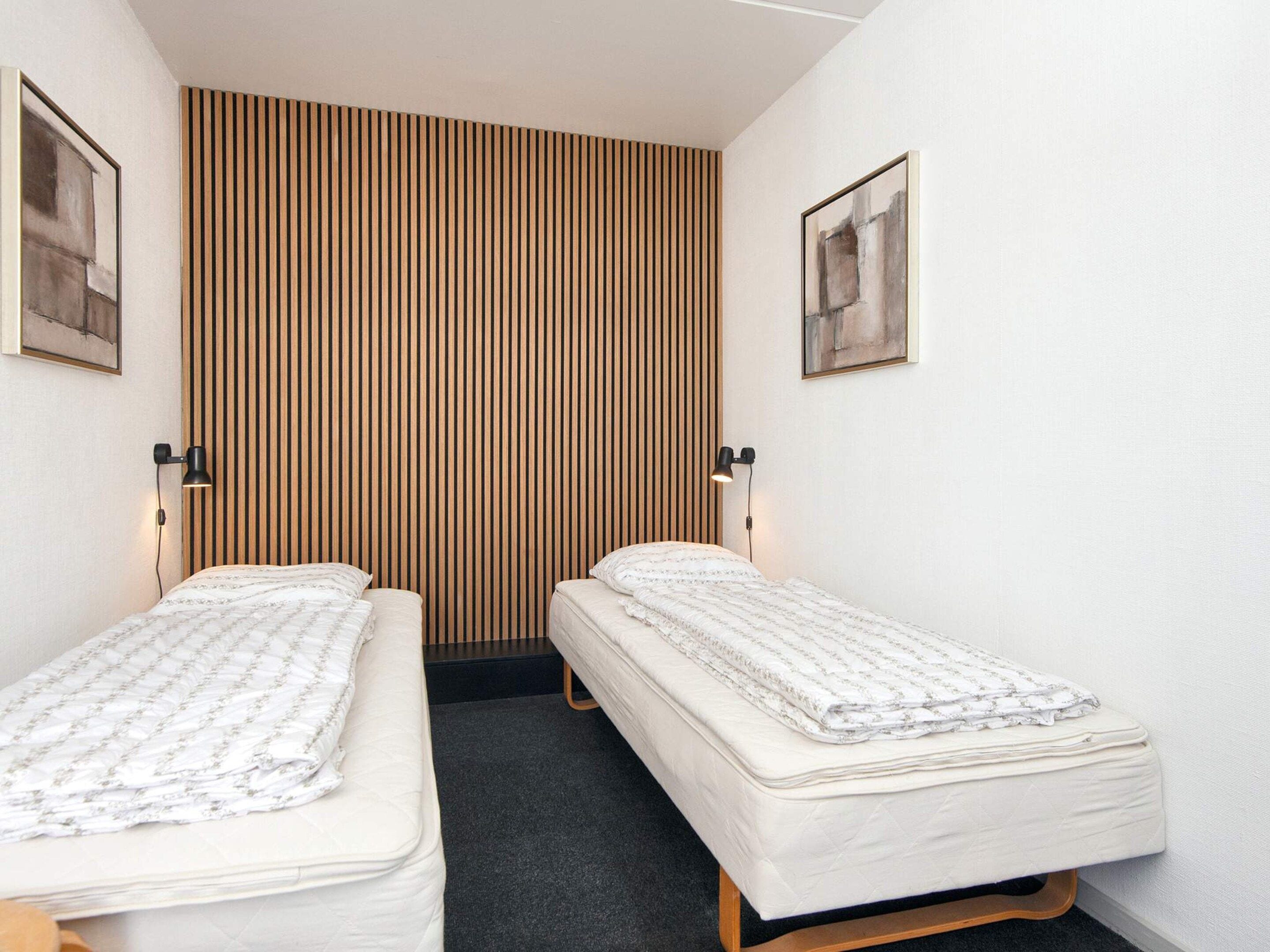 A room with two beds, a wooden slat wall, and two wall-mounted lamps.