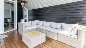 A covered outdoor seating area with a white wicker sofa and a matching ottoman, a metal heater, and a glass door leading to an interior space. - 5 Star Holiday Home in Hadsund (Hadsund)