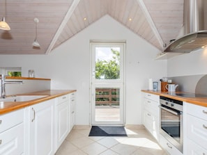 A kitchen with white cabinets, wooden countertops, a stainless steel range hood, and a window with a view of greenery outside. - 5 Star Holiday Home in Hadsund (Hadsund)