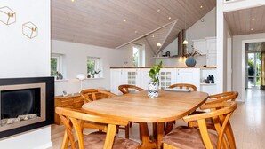 A spacious dining area with a wooden table and chairs, a fireplace, and a view of the kitchen and living area. - 5 Star Holiday Home in Hadsund (Hadsund)