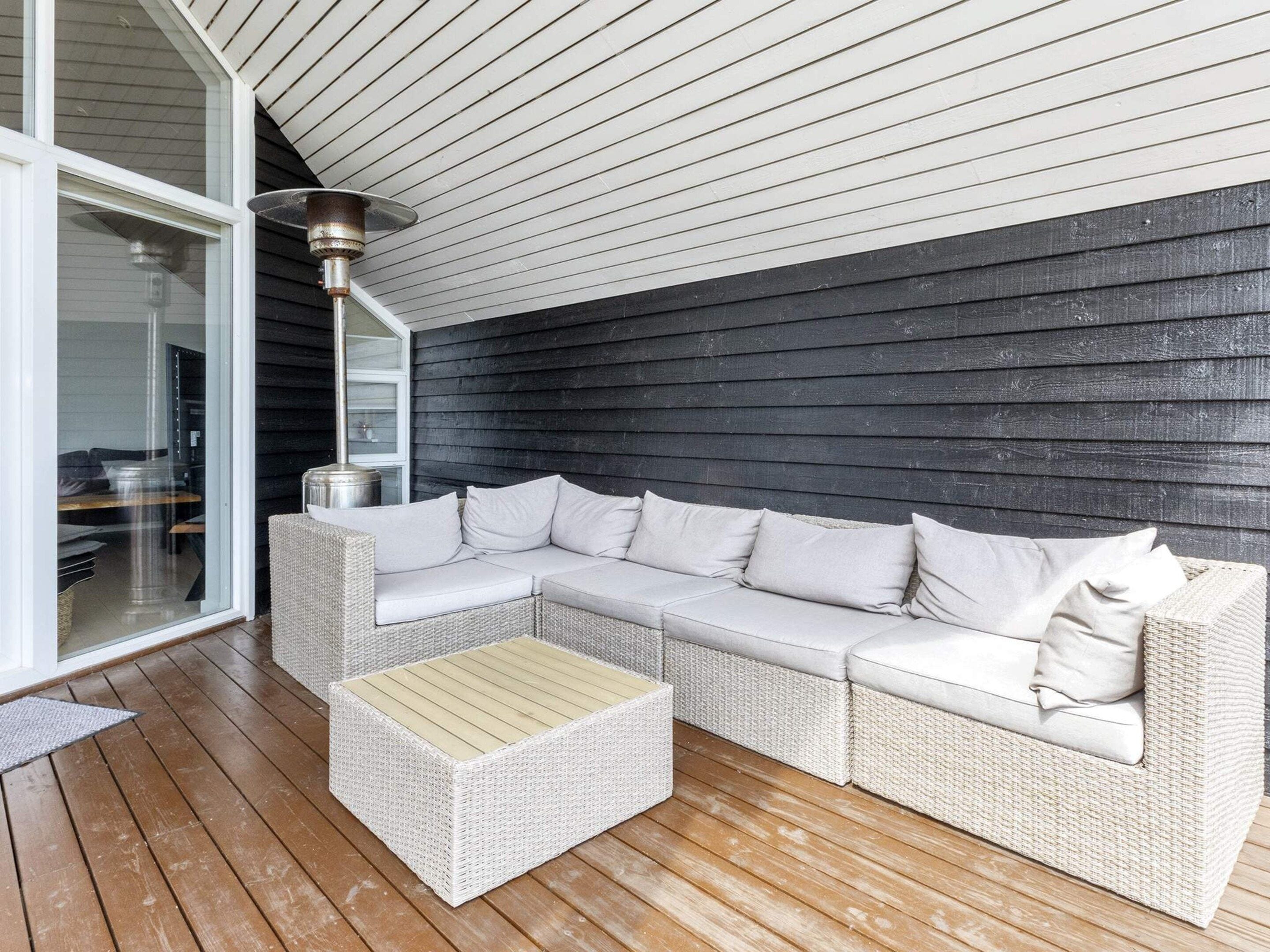 A covered outdoor seating area with a white wicker sofa and a matching ottoman.