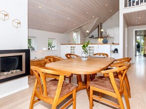 A spacious dining area with a wooden table and chairs, a fireplace, and a view of the kitchen and living area. - 5 Star Holiday Home in Hadsund (Hadsund)