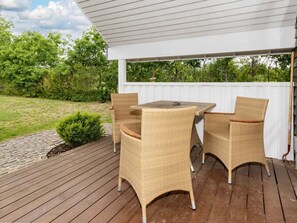 A covered outdoor patio with a wooden deck, wicker furniture, and a white fence. - 5 Star Holiday Home in Hadsund (Hadsund)