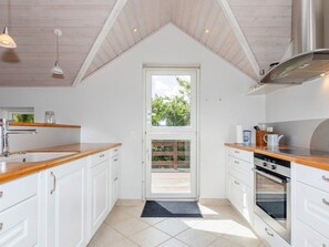 A kitchen with white cabinets, wooden countertops, a stainless steel range hood, and a window with a view of greenery outside.