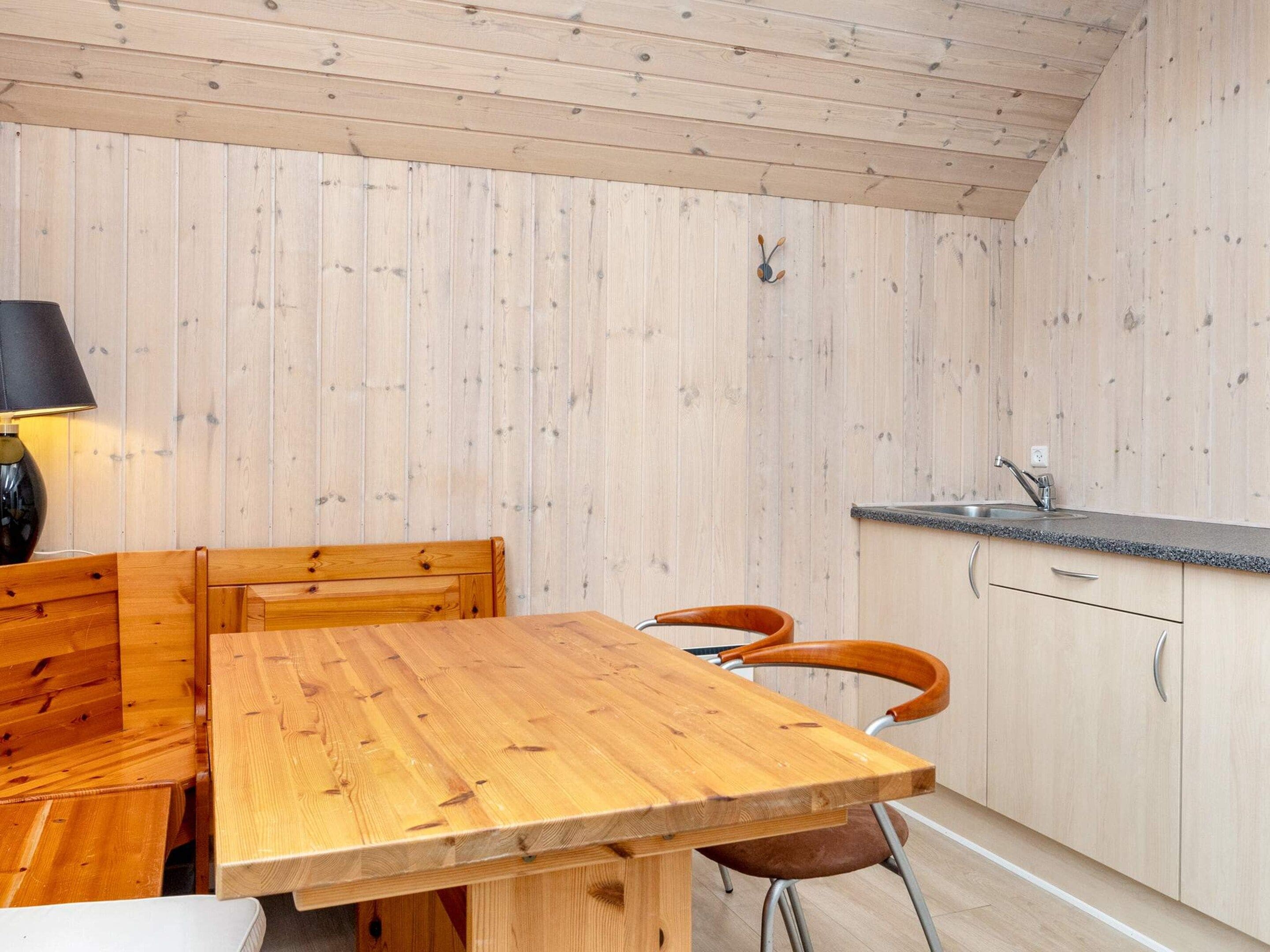 A wooden interior with a dining table, chairs, a lamp, and a kitchen area with cabinets and a countertop.