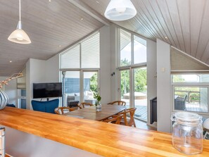 A modern kitchen with a wooden countertop, a dining area with a table and chairs, a television, and large windows. - 5 Star Holiday Home in Hadsund (Hadsund)