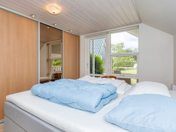 A bedroom with a bed, a window, and a door leading to another room.