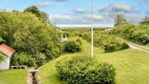 A grassy area with a stone-lined stream, a white building with a red roof, and dense greenery. - 5 Star Holiday Home in Hadsund (Hadsund)