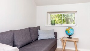 A room with a grey sofa, a small wooden side table with a globe, a window with a view of trees, and a white wall. - 5 Star Holiday Home in Hadsund (Hadsund)