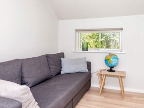 Une pièce avec un canapé gris, une petite table d’appoint en bois sur laquelle se trouve un globe terrestre, une fenêtre donnant sur des arbres et un mur blanc.
