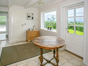 A room with a wooden table, a white door, a window with a view, and a small cabinet with decorative items. - 4 Star Holiday Home in Asperup (Middelfart)