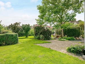Ein gepflegter Garten mit einem gepflasterten Weg, ordentlich geschnittenen Hecken und verschiedenen Bäumen.