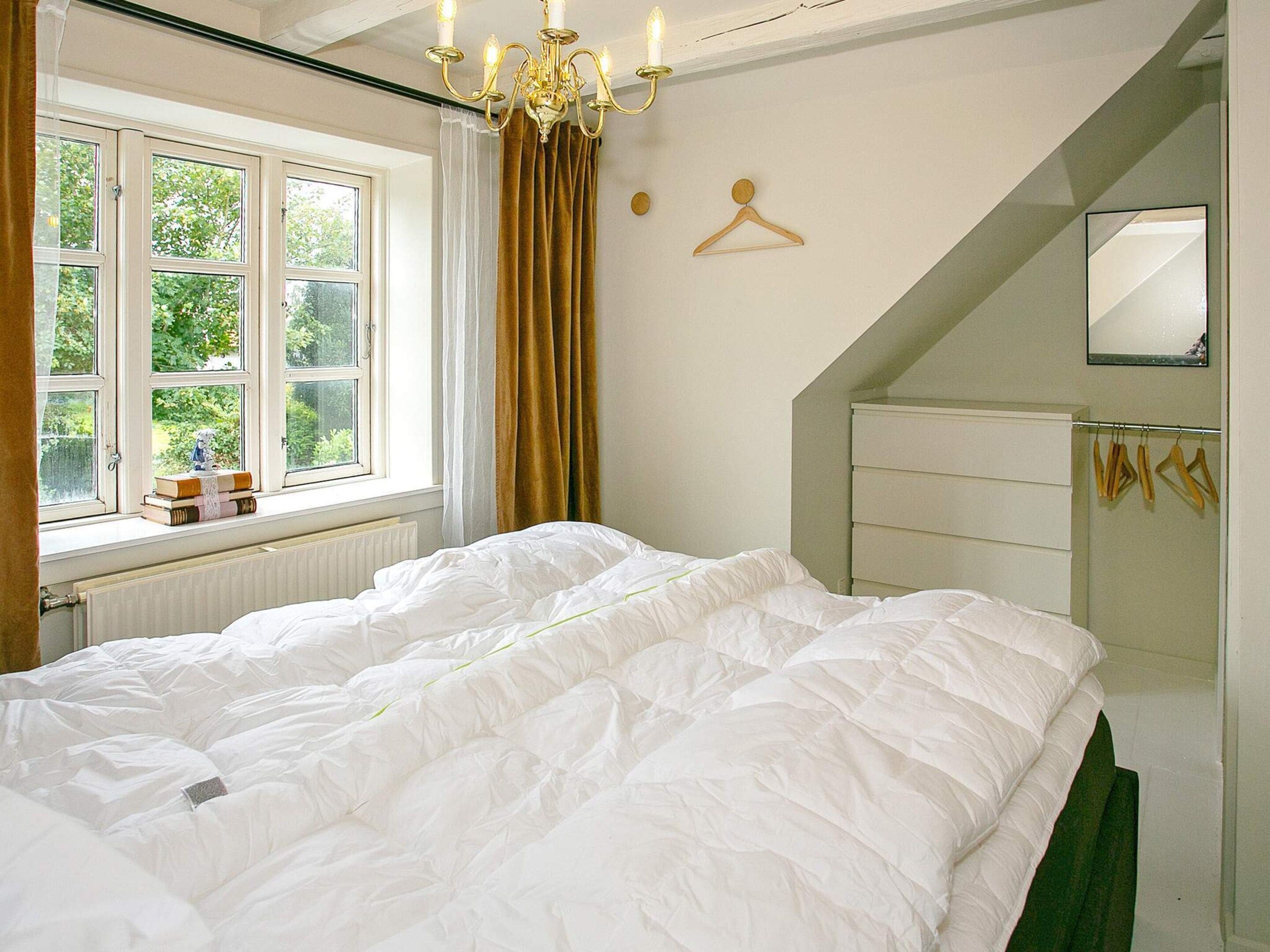 Ein Schlafzimmer mit einem großen Bett, einem Fenster mit Vorhängen, einer Chandelier, einem Spiegel und einer Heizung.