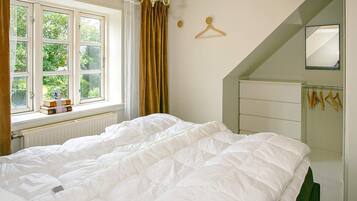 A bedroom with a large bed, a window with curtains, a chandelier, a mirror, and a radiator.