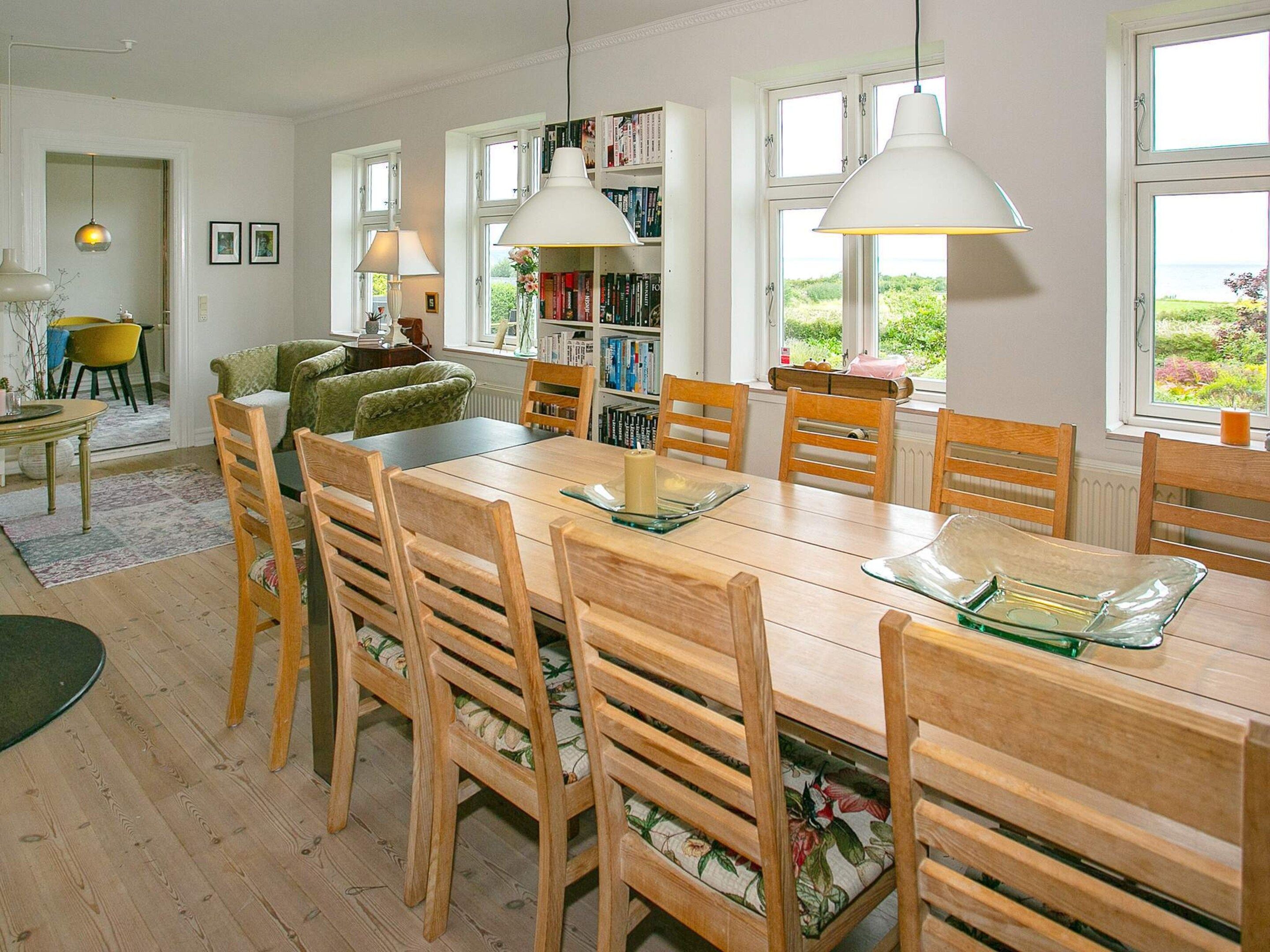 A dining area with a wooden table and chairs, a bookshelf, and a view through the windows.