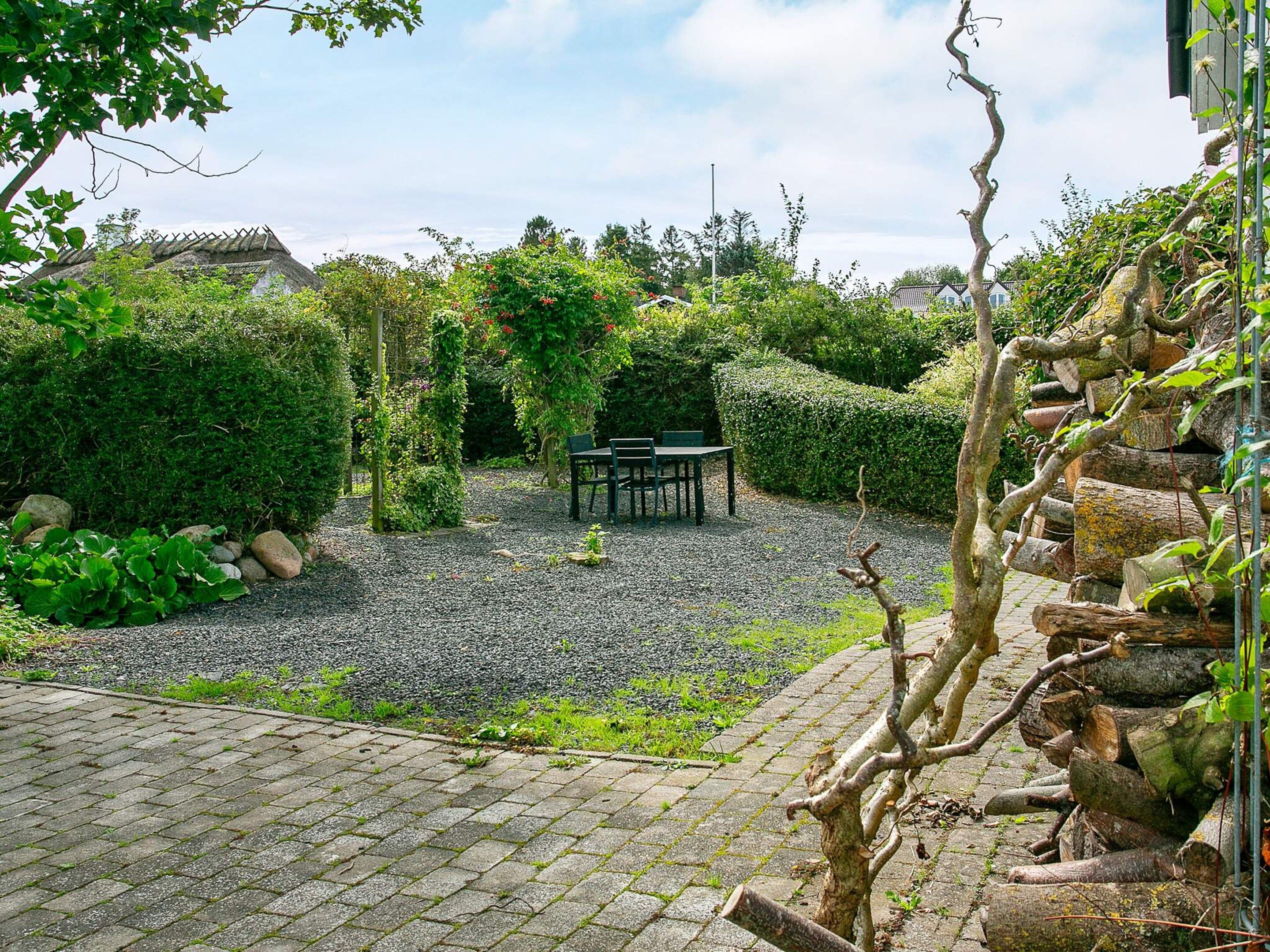 Un jardín con un sendero de grava, un banco de madera y una mesa.