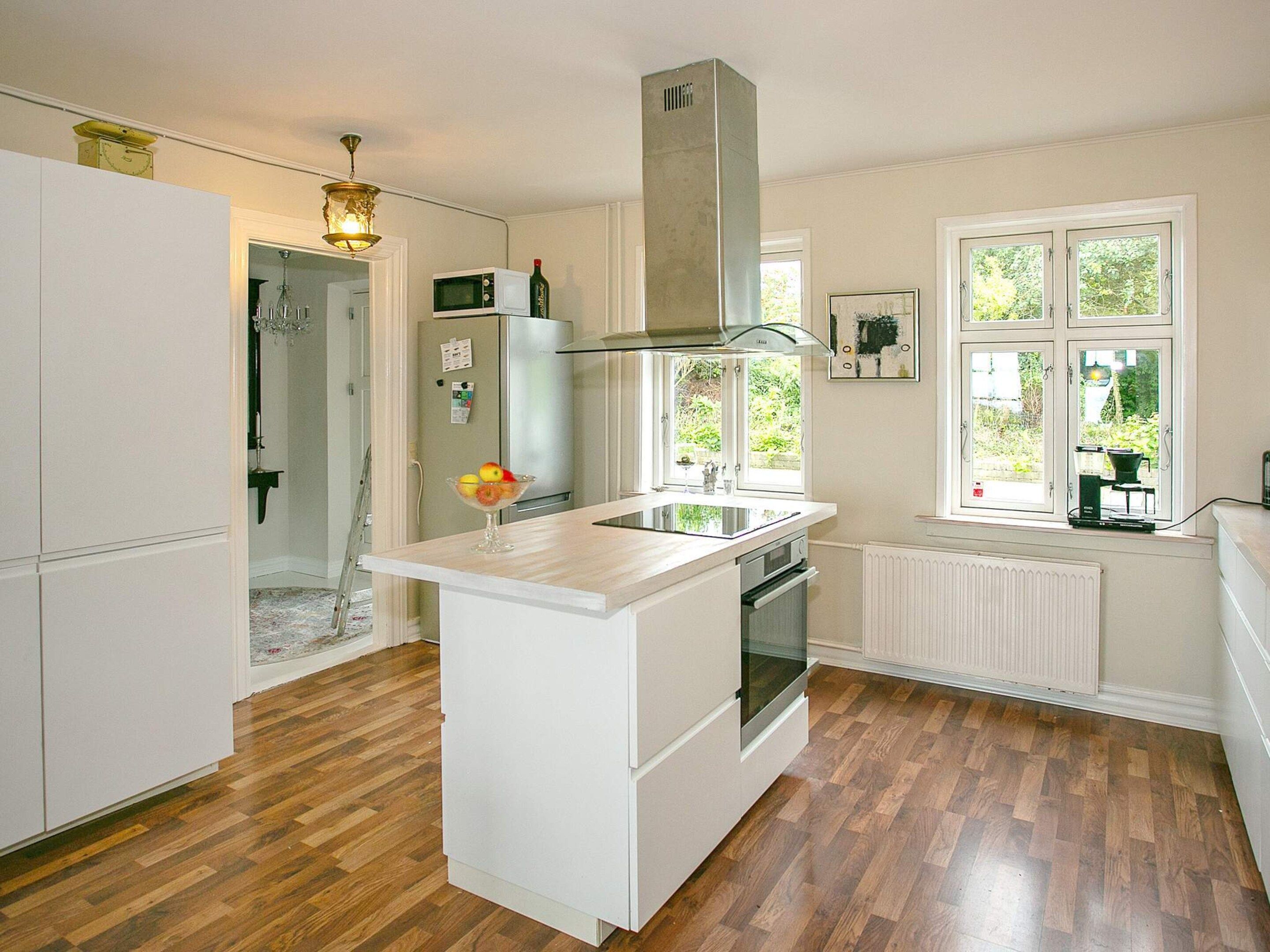 A kitchen with white cabinetry, a central island, a built-in oven, a microwave, and a window with a view of greenery.