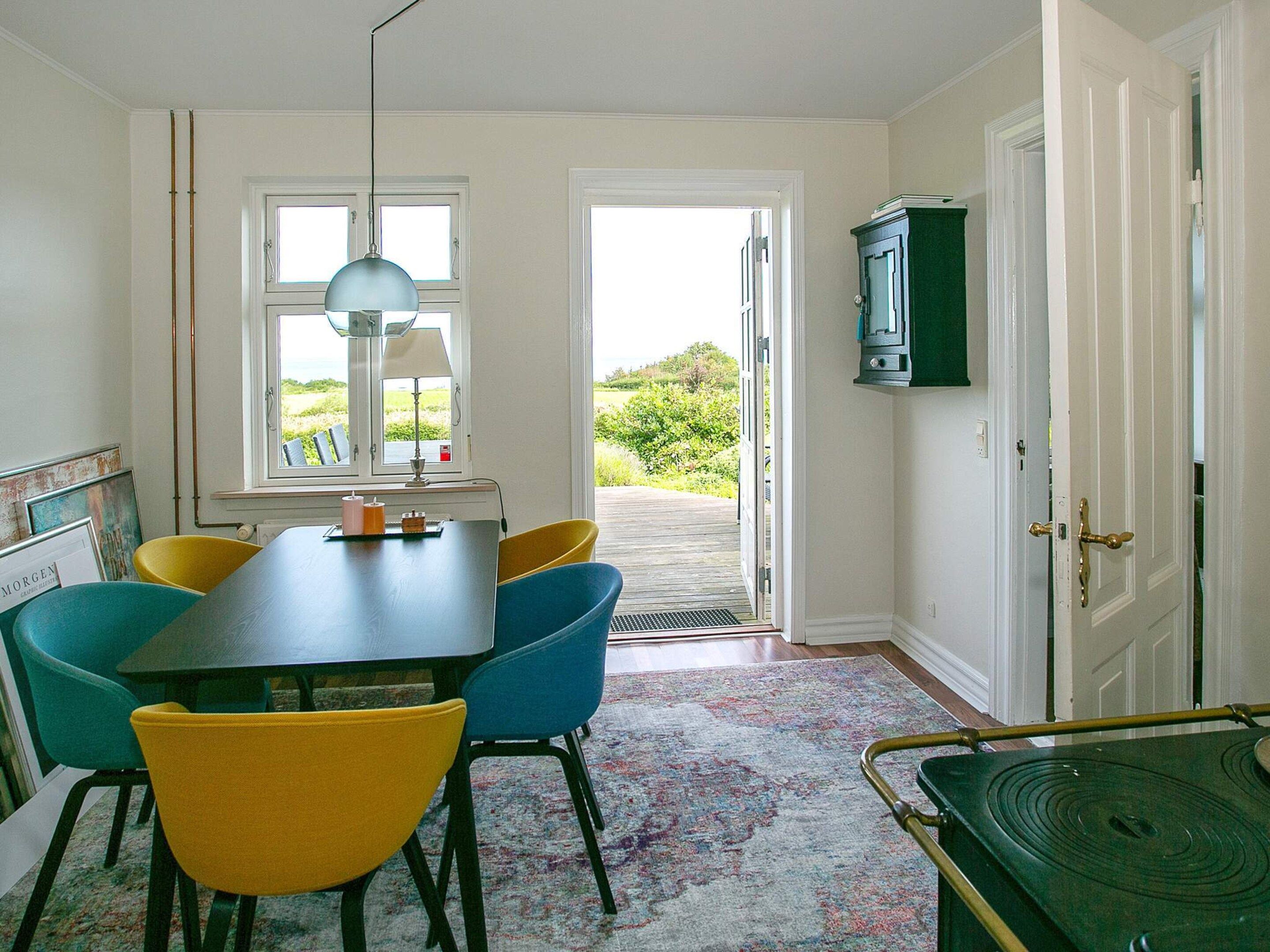 A dining area with a table, chairs, a lamp, and a view through an open door.