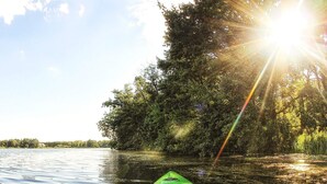 Een groene kajak op kalm water, met een bebosten oever en zonlicht dat door de bomen schijnt.