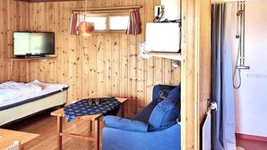 Een kamer met houten lambrisering, een bed, een blauwe bank, een klein tafeltje, een televisie en een verwarming.
