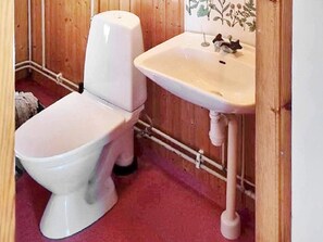 A small, compact bathroom with a white toilet and sink, wooden walls, and visible plumbing.