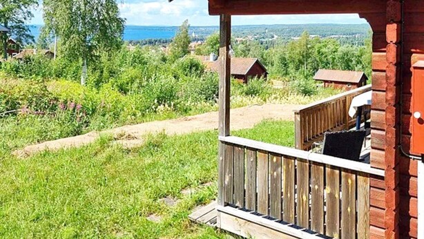 Een houten chalet met een balkon dat uitkijkt over een gazon en gebouwen in de verte.